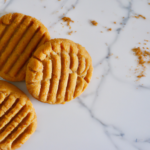 stack of peanut butter cookies on a white marble surface with cookie crumbs nearby